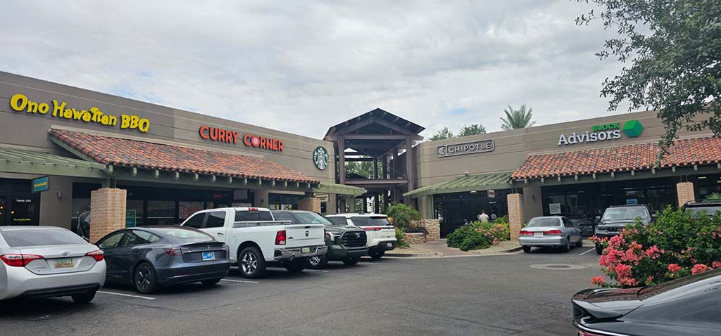 A shopping center featuring restaurants like Ono Hawaiian BBQ, Curry Corner, Starbucks, and Chipotle, with parked cars in the foreground.