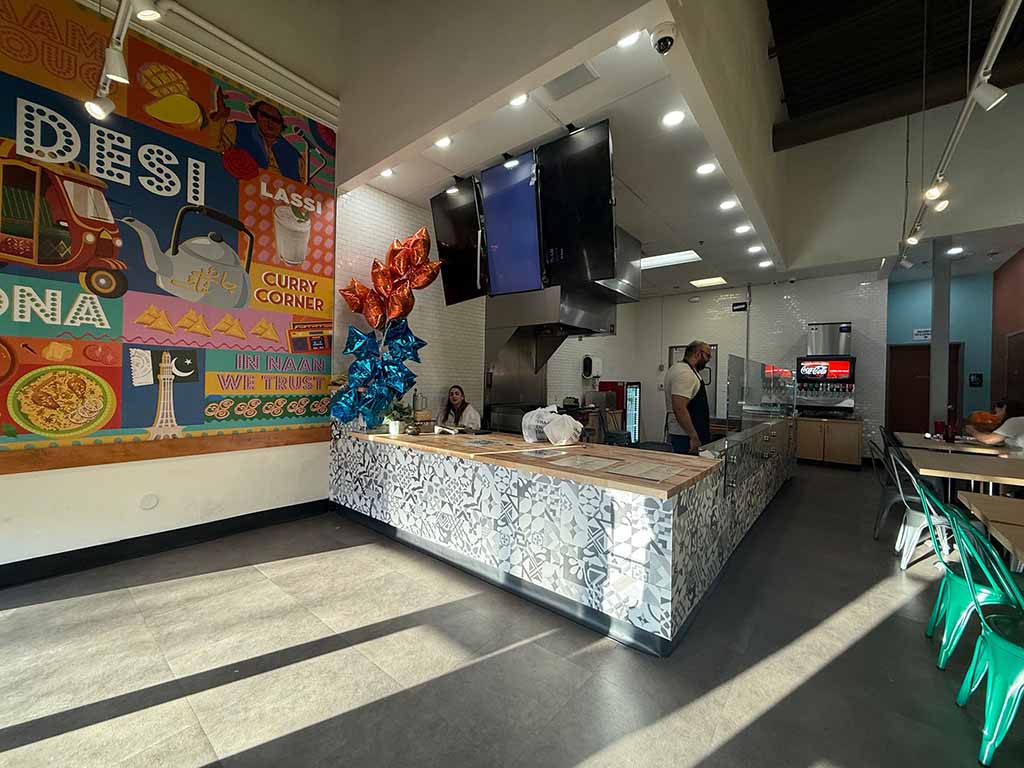 A modern restaurant interior with a colorful mural, a cooking station, and two workers behind the counter.