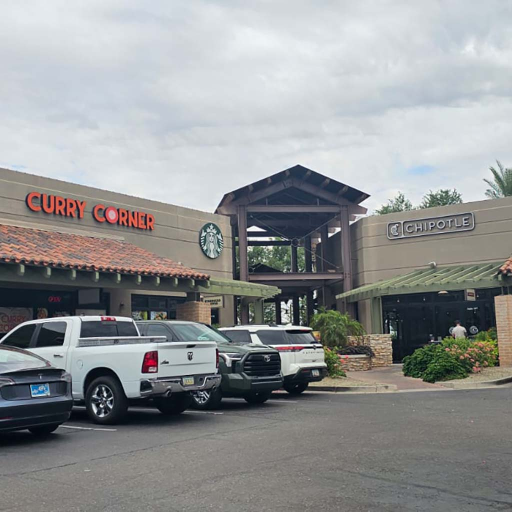 A shopping plaza featuring Curry Corner, Starbucks, and Chipotle restaurants, with parked cars in front.