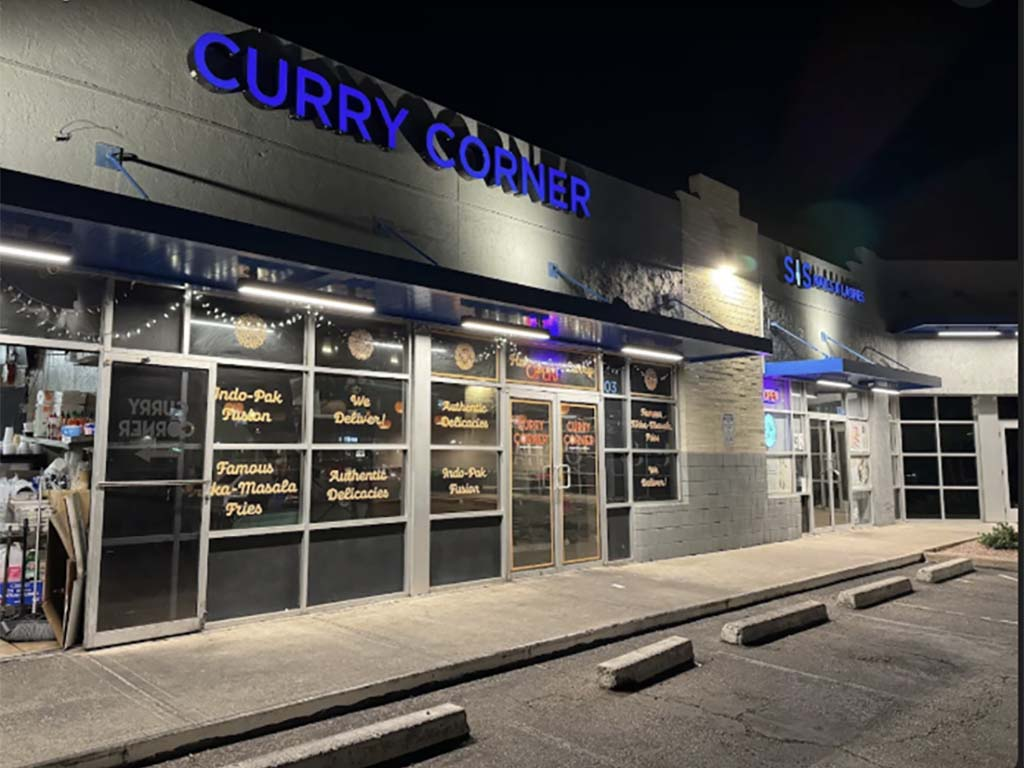 Nighttime exterior of a restaurant called "Curry Corner," with bright blue signage and a menu displayed in the windows
